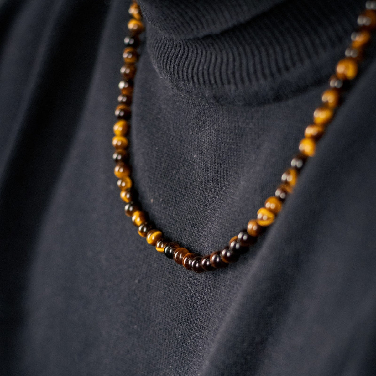 Golden Gaze Necklace (6mm) gedragen over een zwarte col, tijgeroog kralen close-up | Stoney Bracelets