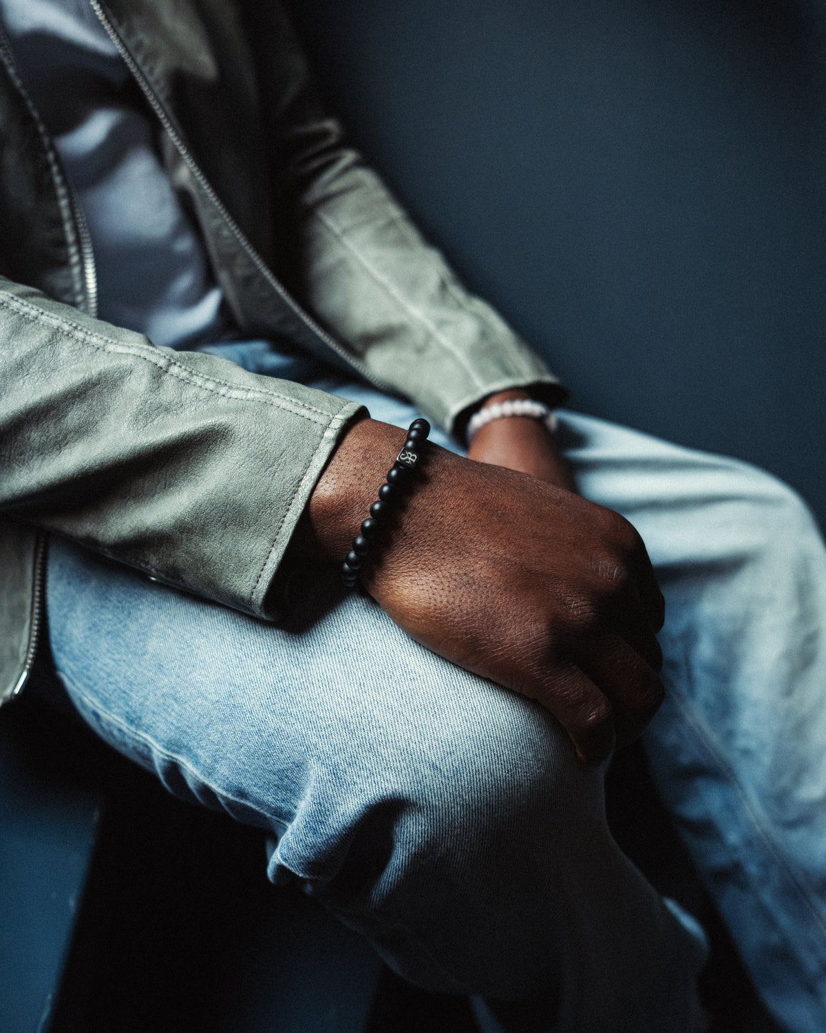 Tattooed arm resting on concrete, wearing a white and a green-black beaded bracelet