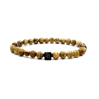 Een Stoney Bracelets Matte Desert Jaspis Stones (6mm) armband met ronde, lichtbruin gemarmerde kralen en een centrale zwarte vierkante "SB"-gegraveerde kraal, afgebeeld op een witte achtergrond.