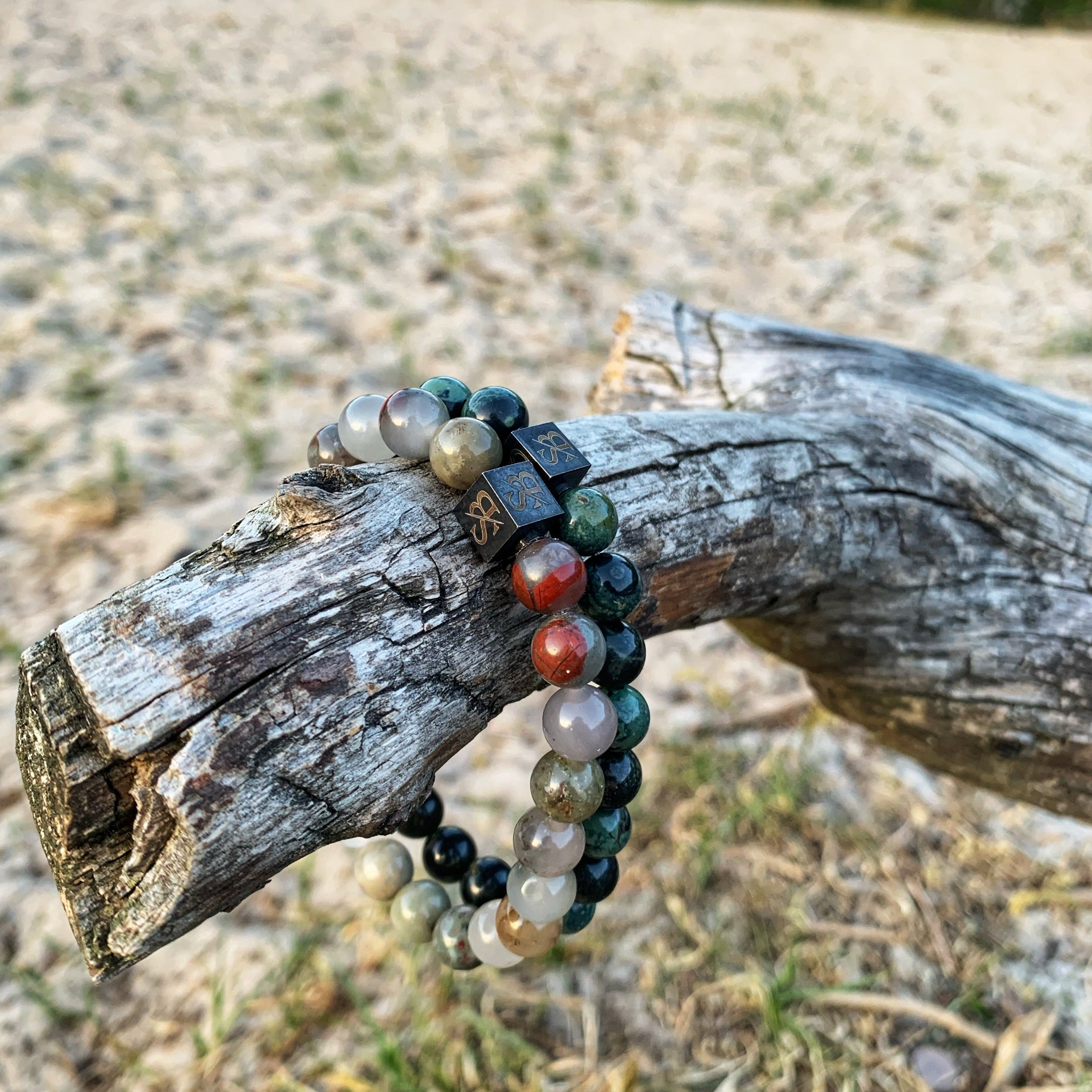 Een Stoney Bracelets Serpent Set (8mm) armband ligt op een boomstam op het strand.