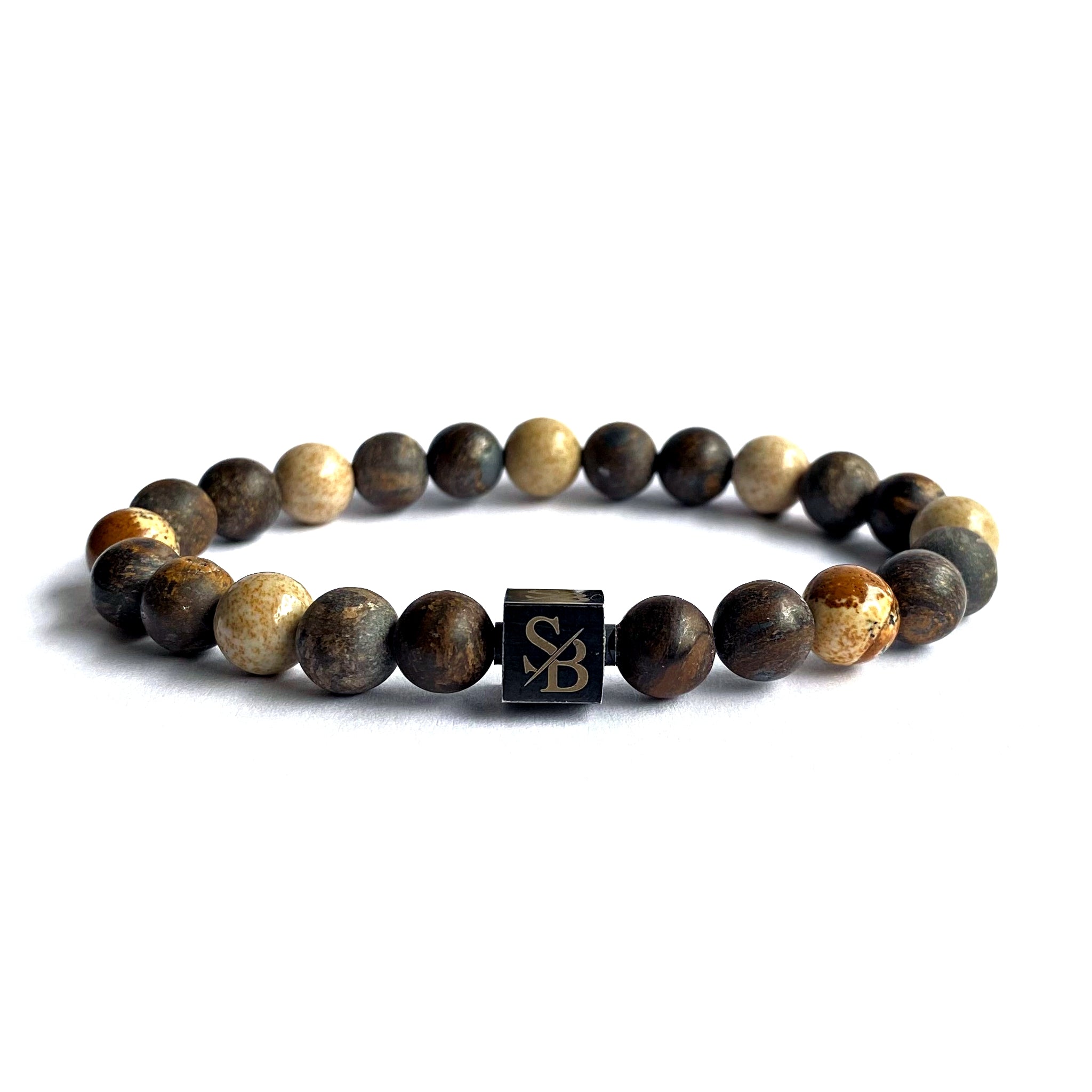 De Desert armband van Stoney Bracelets heeft ronde, gepolijste bruine en beige kralen, een zwart vierkant logo-bedeltje en is elastisch voor unisex draagcomfort. Stijlvol geschikt op een witte achtergrond.